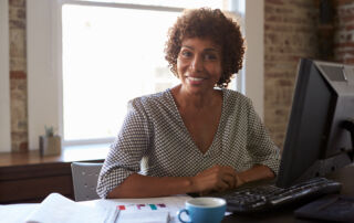 A middle-aged woman smiling at her desk, demonstrating how parents can help sororities and fraternities from home.