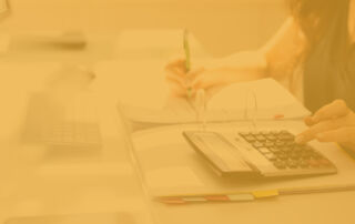 A yellow overlay of the post's feature image, which shows an image of a person using a calculator and writing on a spreadsheet.